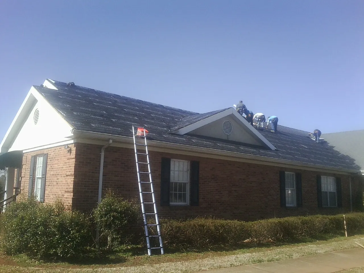 Crew tearing shingles off a brick ranch roof with a ladder set — Emergency Roof Repair work by our crew in Lewes
