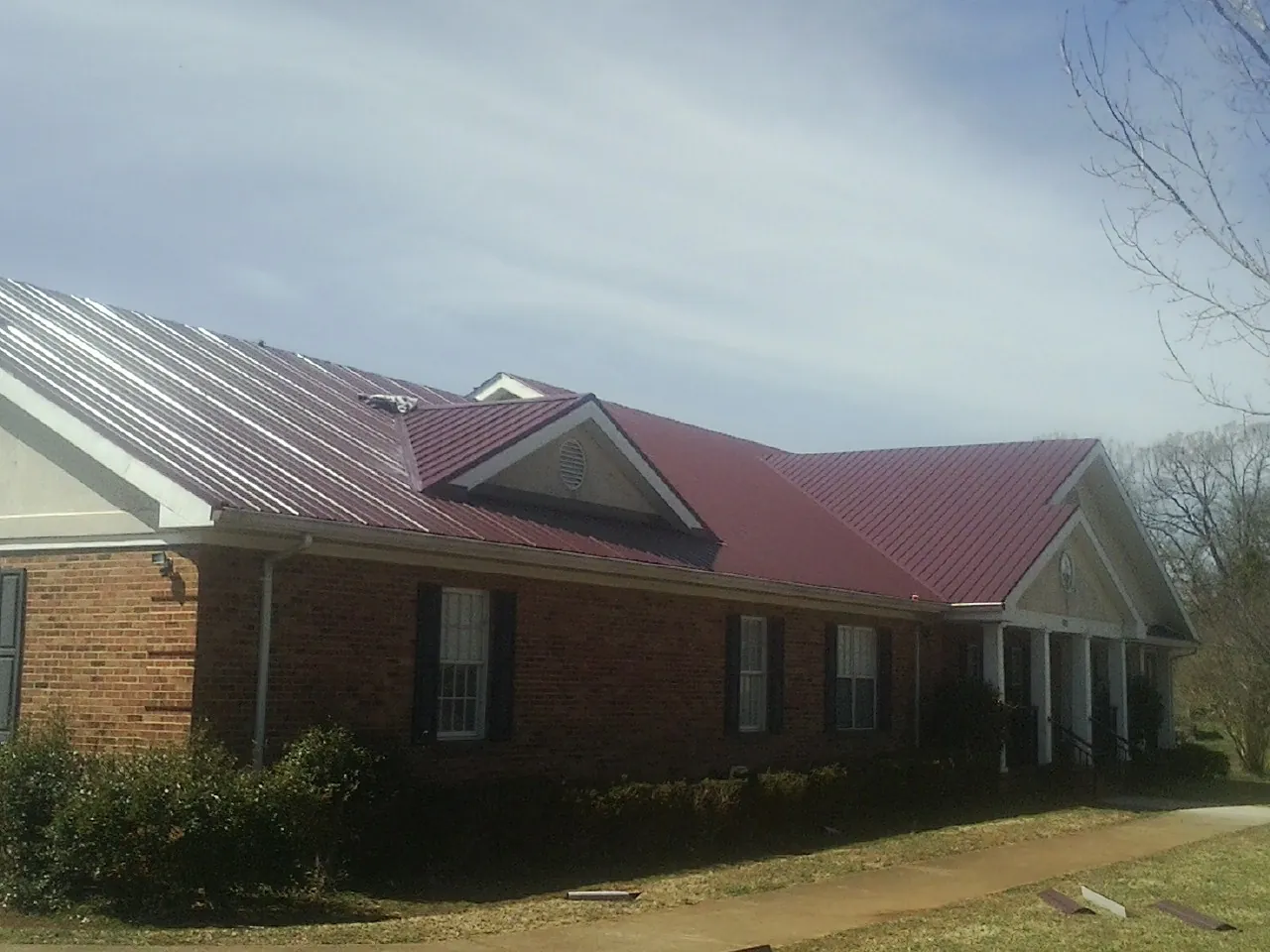 Red metal roof with gabled entries on a long brick building, from a Hail Damage Roof Repair job in Lewes