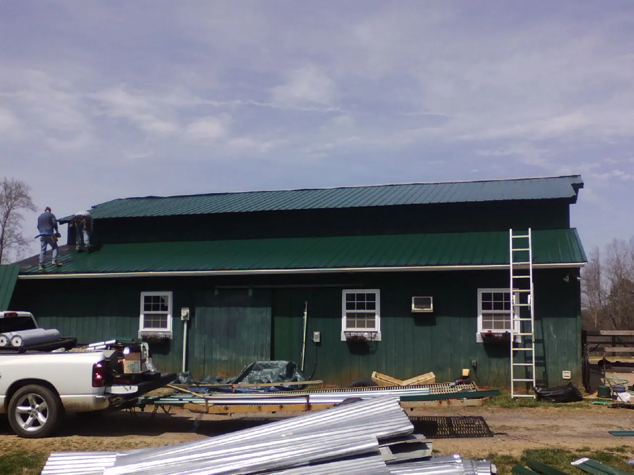 Crew installing green metal roofing on a large green barn in Lewes