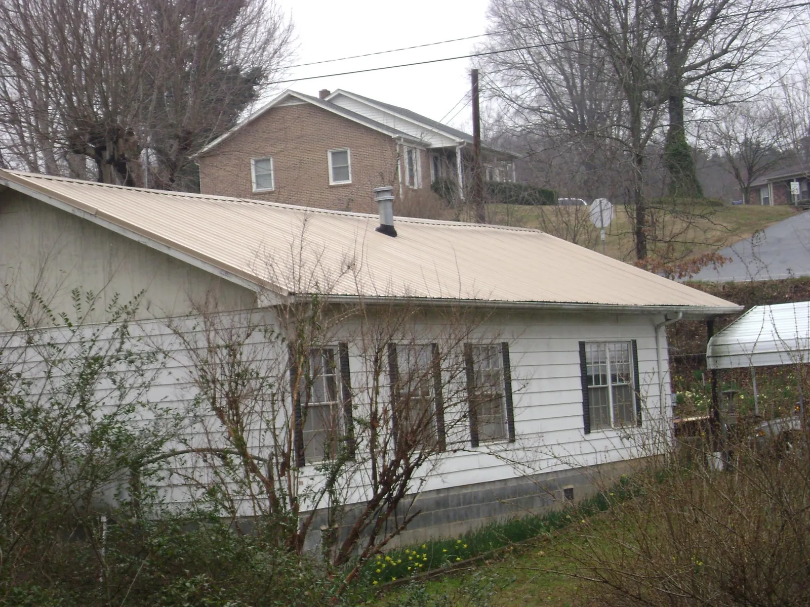 Tan metal roof on a white sided house set into a hillside — Commercial Roofing by Roofing Brothers in Lewes